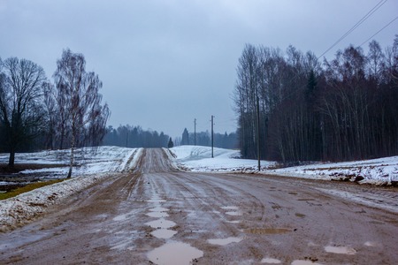 Empty Countryside Landscape in Cloudy Winter Day with Snow Partly Covering the Ground and Fog, Puddles and Tire Marks on the Road - Concept of Sadness and Lonelinessの写真素材