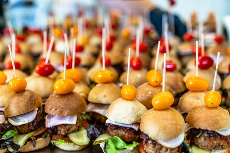 Closeup View of Small Handmade Burgers on the Table with Pickles, Tomatoes, Pork Cutlets and Salads as Ingredients - Kitchen Set, Concept of the Holiday Evening Dinner Tableの写真素材