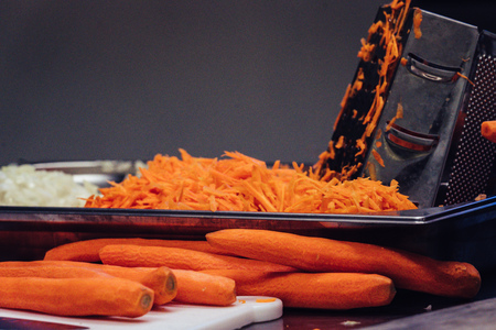 Pealed and Sliced Carrots in a Stainless Steel Bowl on Table - Isolated Object with Blurred Background and Foreground, Kitchen Set with Grater, Vintage Film Lookの写真素材