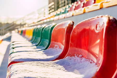 Empty Colorful Football (Soccer) Stadium Seats in the Winter Covered in Snow - Sunny Winter Day with Sun Flare, Concept of Winter Sports and Gameの写真素材