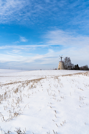 Empty Countryside Landscape in Sunny Winter Day with Snow Covering the Ground with Big Abandoned Windmill in Background - Concept of Fun, Joy and Travelの写真素材