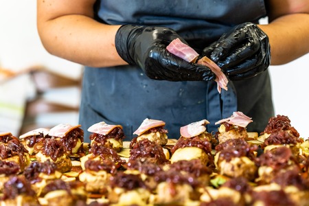 Female Chef Putting Ingredients of Burgers on a Sliced Bread Spread on a Table in Black Gloves - Concept of the Hard Working Person and the Hygiene in the Kitchen, Partly Blurred Backgroundの写真素材