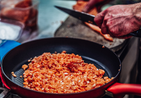 Red Pan with Pile of Cut Salmon Pieces in the Foreground, Male Chef Cutting Fresh Salmon on the...