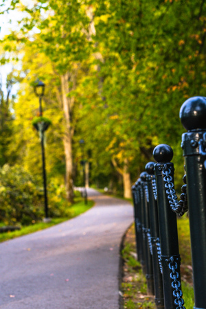 Colorful Photo of the Road in a Park, Between Woods - Closeup view of the Chain Fence with Blurred Background with Space for Text, Sunny Autumn day, Concept of the Peace and Harmonyの写真素材