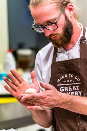 Odziena / Latvia - August 24th, 2018: Male Chef Preparing Bread Dough for Selfmade Bread and Patties - Kitchen Set, Text on Apron "Made to go presents, Great Bakery, Enjoy"のeditorial素材