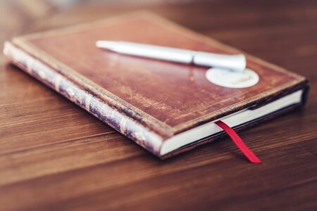 Antique brown notebook on wooden table with white pen and red bookmark, selective focusの写真素材
