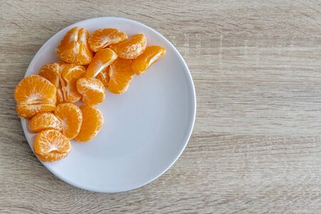 Top down view of pealed mandarin peaces on white plate, wooden desk surface, copy space for textの写真素材