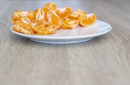 Pealed mandarin peaces on white plate, wooden desk surface, copy space for textの写真素材