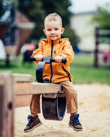 Young caucasian child enjoys swings in park, innocent look in his blue eyesの写真素材