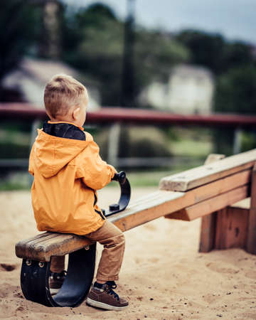Child left alone on swings in the park, from behindの写真素材
