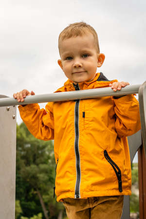 Cute young boy with short blond hair holding to a bar in playgroundの写真素材