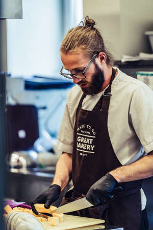 Odziena / Latvia - August 24th, 2018: Male Chef Cutting Pumpkins on Yellow Plastic Board - Kitchen Set, Vertical photoのeditorial素材