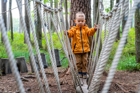 Young Child Playing on Rope Obstacle Track in Woods - Caucasian Boy Wearing Orange Raincoatの写真素材