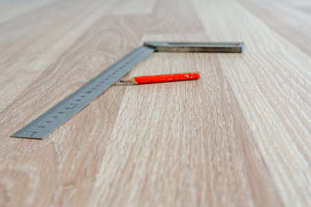 Red Carpenter's Pencil and Right Angle's Tool on Laminate Floor after Renovation or Reconstruction...