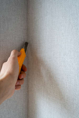 Hand Holding, Cutting Gray Wallpaper Side with Yellow Construction Knife in Corner of Room, Remodeling and Reconstruction Processの写真素材