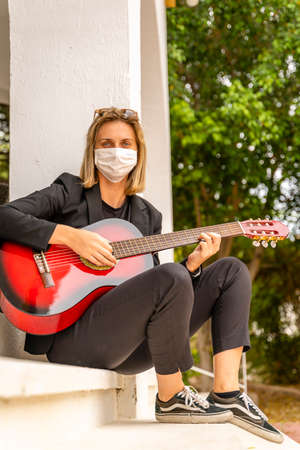 Young Caucasian Girl Wearing White Face Mask, Plays Red Guitar, Mockup. Business Outfitの写真素材