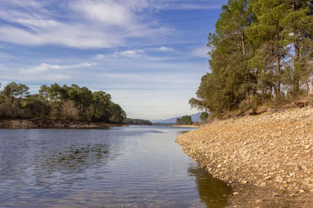 Flow of a river with stones and trees in the shores. Cloudy day.