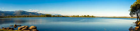 Inland lake with trees and mountains in the background on the shore.の写真素材