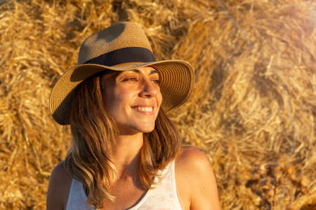 Young girl smiling and enjoying life with a background of hay and mowed wheat wrapped in a harvested haystack. Selective focus. Portrait. Copy space.の写真素材