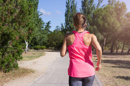 Young woman running through a park on a sunny day while listening to music with headphones. Healthy...
