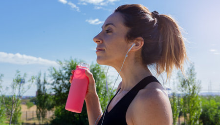 Young woman with water bottle in her hand resting after running while listening to music with headphones. Healthy lifestyle. Selective focus.の写真素材