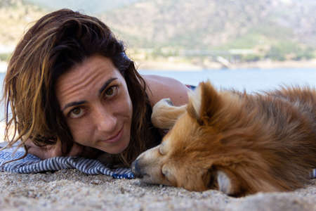 Woman lying on a towel smiling at the camera next to her dog. Selective focus. Copy space.の写真素材