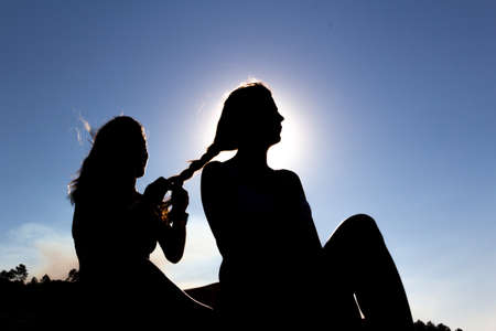Two girls braiding each other's hair against the light. Friendship.の写真素材