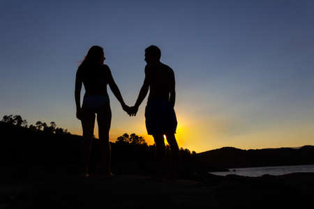 Loving couple holding hands in a romantic sunset on a lake. Autumn. Backlight. Copy space.の写真素材