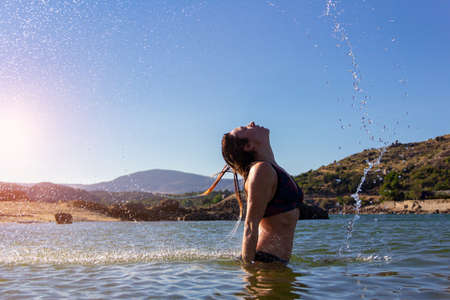 Young girl in a bikini doing a wave with her hair in a lake. Summer. Movement concept. Copy space. Selective focus.の写真素材