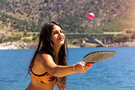 Young girl hitting a ball with a racket on the shore of a lake. Summer sport. Selective focus. Leisure.の写真素材