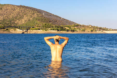 Boy on his back with his hands on his head in the water of a lake. Selective focus. Copy space.