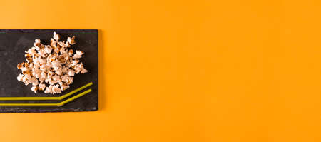 Popcorn on slate tray and soda straws on yellow background. Flat lay. Copy space. Home movie time.