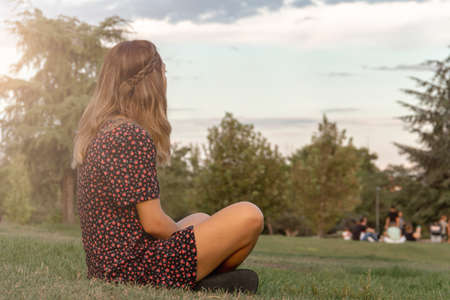 Young woman sitting on the lawn of a park looking at infinity. Selective focus.の写真素材