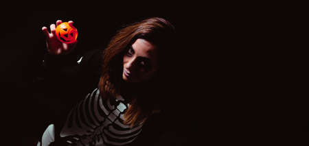 Woman in halloween skeleton costume with toy pumpkin. Night of the dead. Copy space. Selective focus.の写真素材