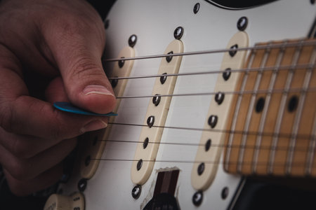 Person plucking the strings of an electric guitar with a pick. Selective focus. Copy space.