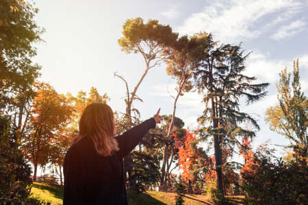 Young woman pointing to trees in autumn. Selective focus.