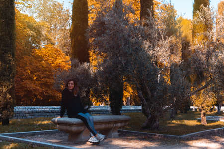 Young woman smiling sitting on a bench in autumn. Selective focus.の写真素材
