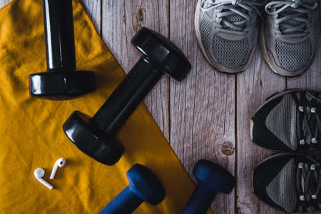 Fitness dumbbells with wireless headphones and sneakers on wooden background. Gym accessories. Copy space. Selective focus.の写真素材