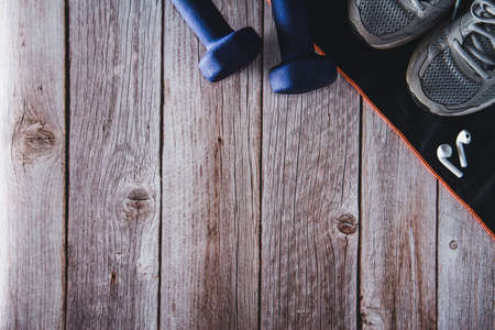 Fitness dumbbells with trainers and headphones on wooden background. Gym accessories. Copy space. Selective focus.の写真素材