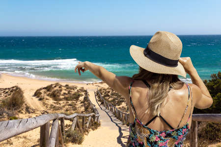 Young woman on her back with a hat pointing to the sea. Copyspace. Selective focus.