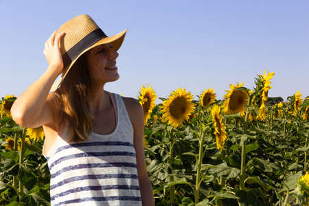 Portrait of young woman with hat in a field of sunflowers. Sunny day. Copyspace. Selective focus.
