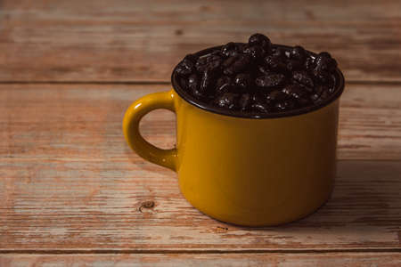 Yellow mug filled with coffee beans on vintage wooden surface. Copyspace. Selective focus.の写真素材