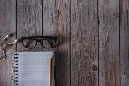 Notebook with pen, headphones and glasses to create on wooden background. Top view. Copyspace. Selective focus.の写真素材