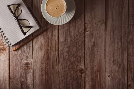 Workspace with notebook, glasses and coffee on wooden background. Top view. Copyspace. Selective...