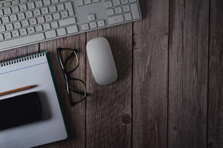 Workspace with computer keyboard, notebook, glasses and smartphone on wooden background. Top view....