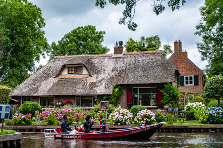 Giethoorn, Netherlands - July 6, 2019: Tourists on a motorboat navigating the canals of Giethoorn, also known as the Venice of Netherlandsのeditorial素材