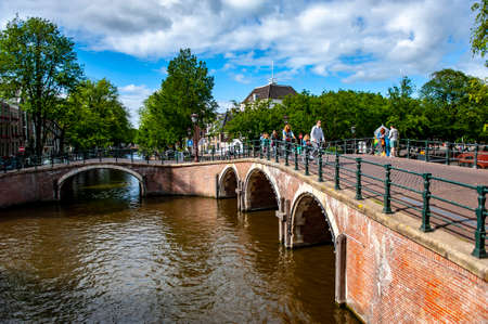 Amsterdam, Netherlands - July 7, 2019: People walking and cycling on a red brick bridge above the canals of Amsterdam in the Netherlandsのeditorial素材