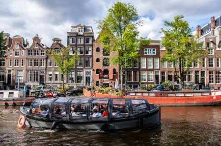 Amterdam, Netherlands - July 7, 2019: Touristic boat navigating the canals of Amsterdam in the Netherlands on a summer dayのeditorial素材