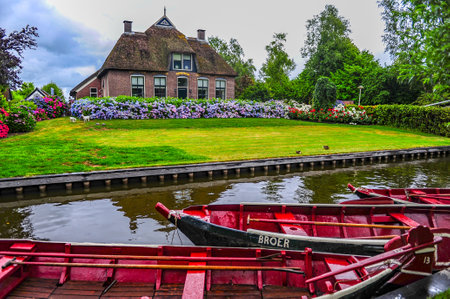 Giethoorn, Netherlands - July 6, 2019: Red boats docked in the canal in front of a typical Dutch rural house in the village of Giethoorn, the Netherlandsのeditorial素材