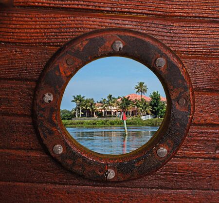 Unusual rustic porthole view of beautiful palms, riverfront homes and river.の写真素材